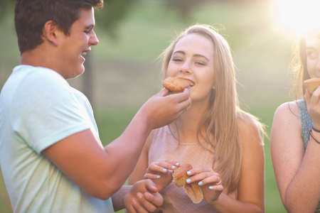 Boy feeding girl, friend in backgroundの写真素材