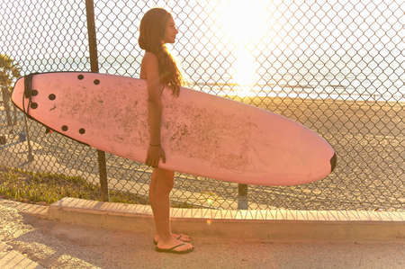 Girl standing at beach holding pink surfboardの写真素材