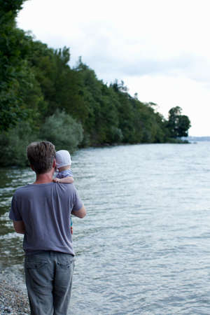 Father holding baby daughter by lake, Starnberg, Germanyの写真素材