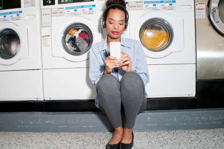 Young woman in launderette, wearing headphones, waiting for laundry to finish
