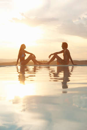 Couple sitting on infinity poolside in sunlightの写真素材