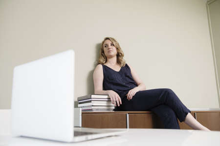 Young businesswoman sitting on cupboard in new office
