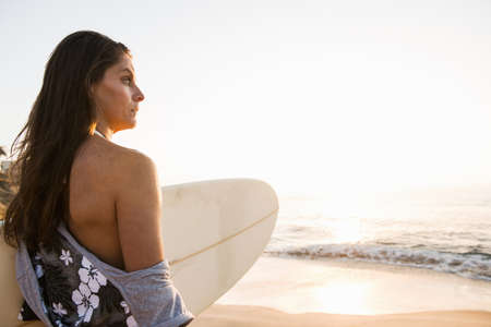 Surfer carrying surf board, looking at seaの写真素材