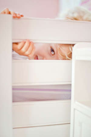 Close up portrait of four year old boy peeking through bed frame