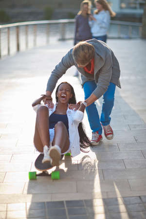 Young couple fooling around on skateboard at riverside