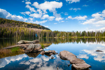 Hiker on pathway of rocks, surrounded by reflections of clouds, on Quinescoe Lake, Cathedral Lakes...