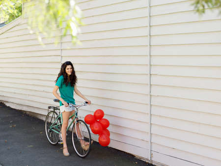 Portrait of young woman with bicycle and a bunch of balloonsの写真素材