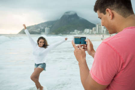 Young couple photographing with smartphone on Ipanema Beach, Rio de Janeiro, Brazilの写真素材