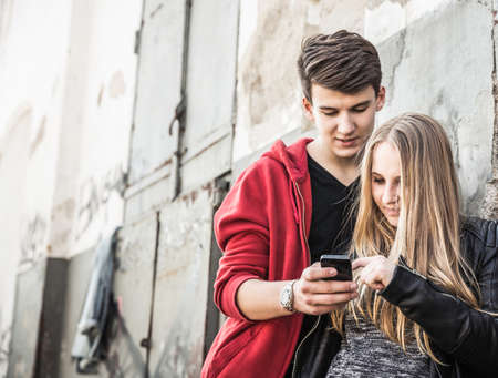 Teenage couple using smartphone by abandoned buildingの写真素材