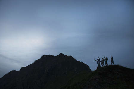 Silhouette of four young adult men with arms raised on top of mountain