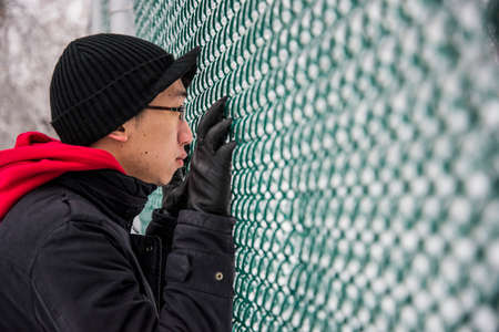 Portrait of young man looking through park fence at -30 degrees celciusの写真素材