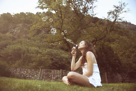 Young woman sitting cross legged in field blowing bubblesの写真素材