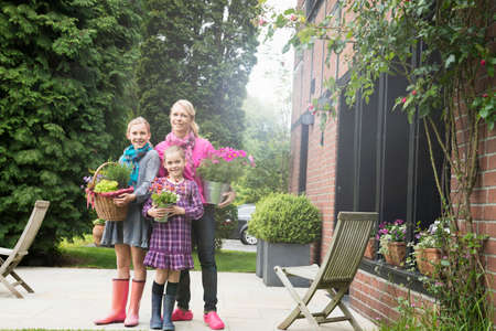 Mother and daughters outside house holding plants