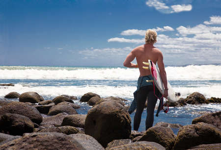 Young adult male surfer watching sea from beach rocksの写真素材