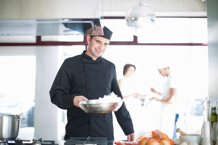 Male chef carrying frying pan in commercial kitchenの写真素材