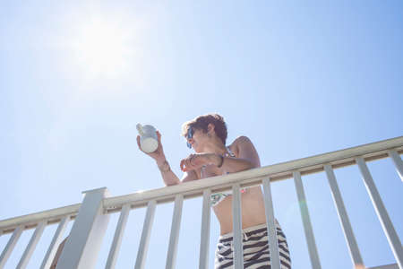 Low angle view of mid adult woman leaning against balcony with coffee mug