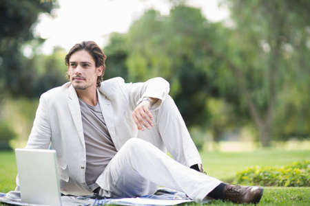 Businessman reclining on picnic blanket using laptop in parkの写真素材