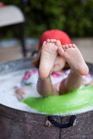 Girl sitting in bubble bath in garden with feet sticking outの写真素材