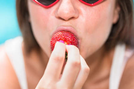 Cropped portrait of young woman biting strawberryの写真素材