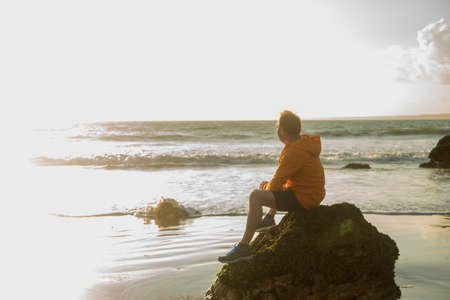 Mature man, sitting on rock, looking out to sea