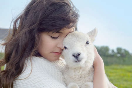 Portrait of young woman in field carrying lamb wrapped in blanket