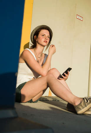 Young woman sitting outside building with smartphoneの写真素材