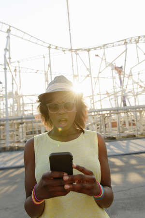 Young woman looking surprised at smartphone, Coney Island, Brooklyn, New York, USAの写真素材