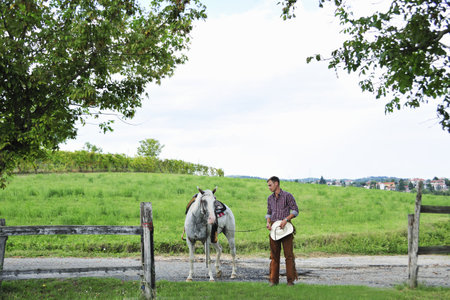 Young man in cowboy gear leading horse through gatewayの写真素材