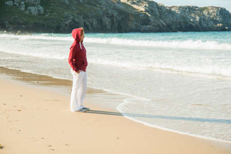 Mature woman standing on beach with hands in pockets, Camaret-sur-mer, Brittany, Franceの写真素材