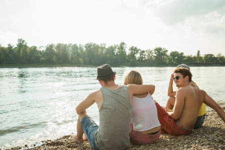 Four young friends sitting on lakeshoreの写真素材