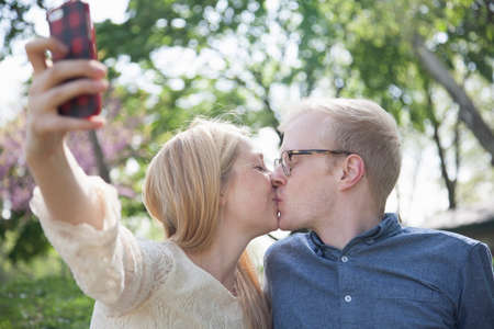 Young couple in park taking selfie whilst kissingの写真素材