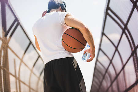 Rear view of young male basketball player walking along footbridge listening to headphonesの写真素材