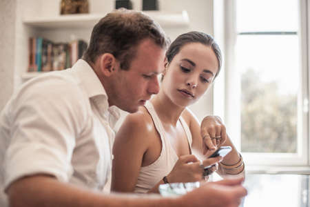 Young couple looking at smartphone at kitchen tableの写真素材