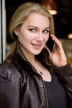 Young woman chatting on smartphone in cafe doorwayの写真素材