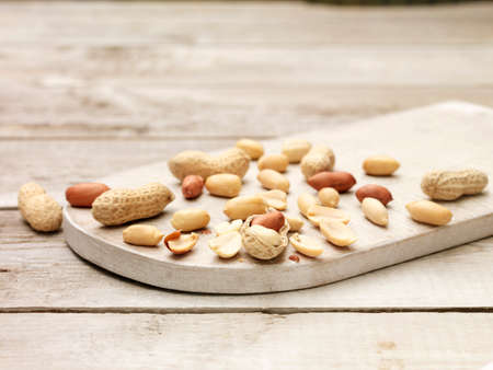 Peanuts, whole and cracked open monkey nuts on wooden chopping boardの写真素材