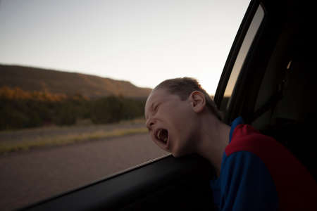 Boy leaning out of car window with eyes closed and mouth openの写真素材