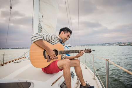 Young man on sailing boat playing guitarの写真素材