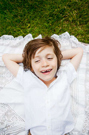 Boy lying on tablecloth on grass with hands behind headの写真素材