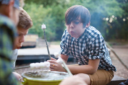 Group of young boys toasting marshmallows over bucket barbecueの写真素材