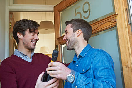 Men with bottle of wine smiling at front doorの写真素材