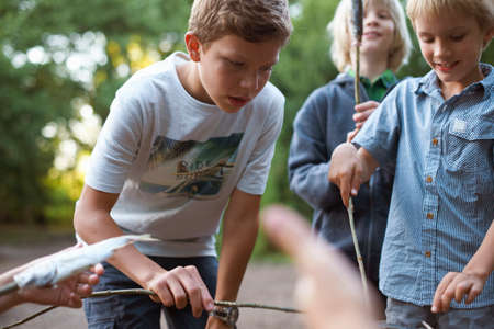 Young boys cooking fish over barbecueの写真素材