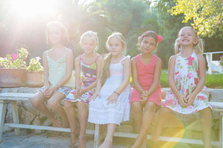 Portrait of five girls sitting on garden benchの写真素材