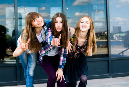 Three young women leaning forward in a row and making I love you hand gesture