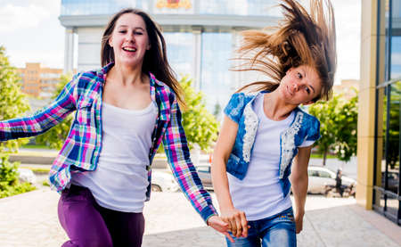Two young women shaking their hair and running in cityの写真素材