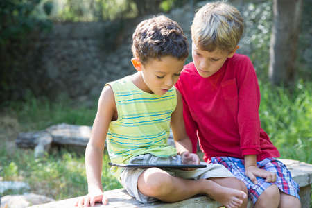 Two boys sitting on garden seat looking down at digital tabletの写真素材