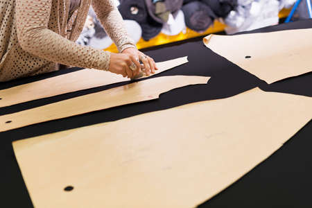 Hands of mature seamstress chalking shape onto textile on work table