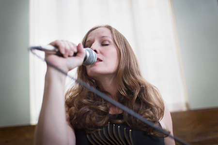 Close up of mature woman singing with microphone in hallの写真素材