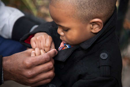 Close up of male toddler buttoning jacket  in park