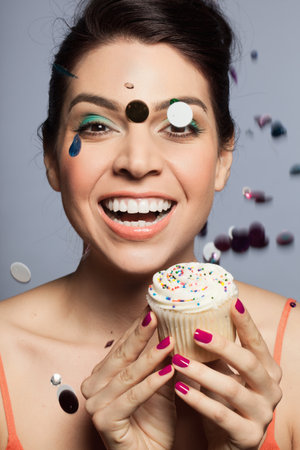 Mid adult woman holding cupcake with glitter falling on front of faceの写真素材