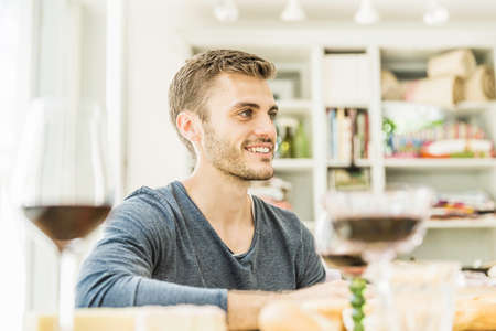 Young man drinking wine at table in dining roomの写真素材